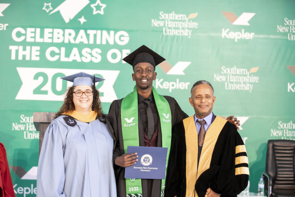 College graduate posing with diploma alongside faculty