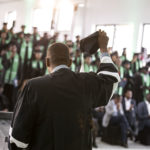 Man holding regalia cap out to crowd of graduates