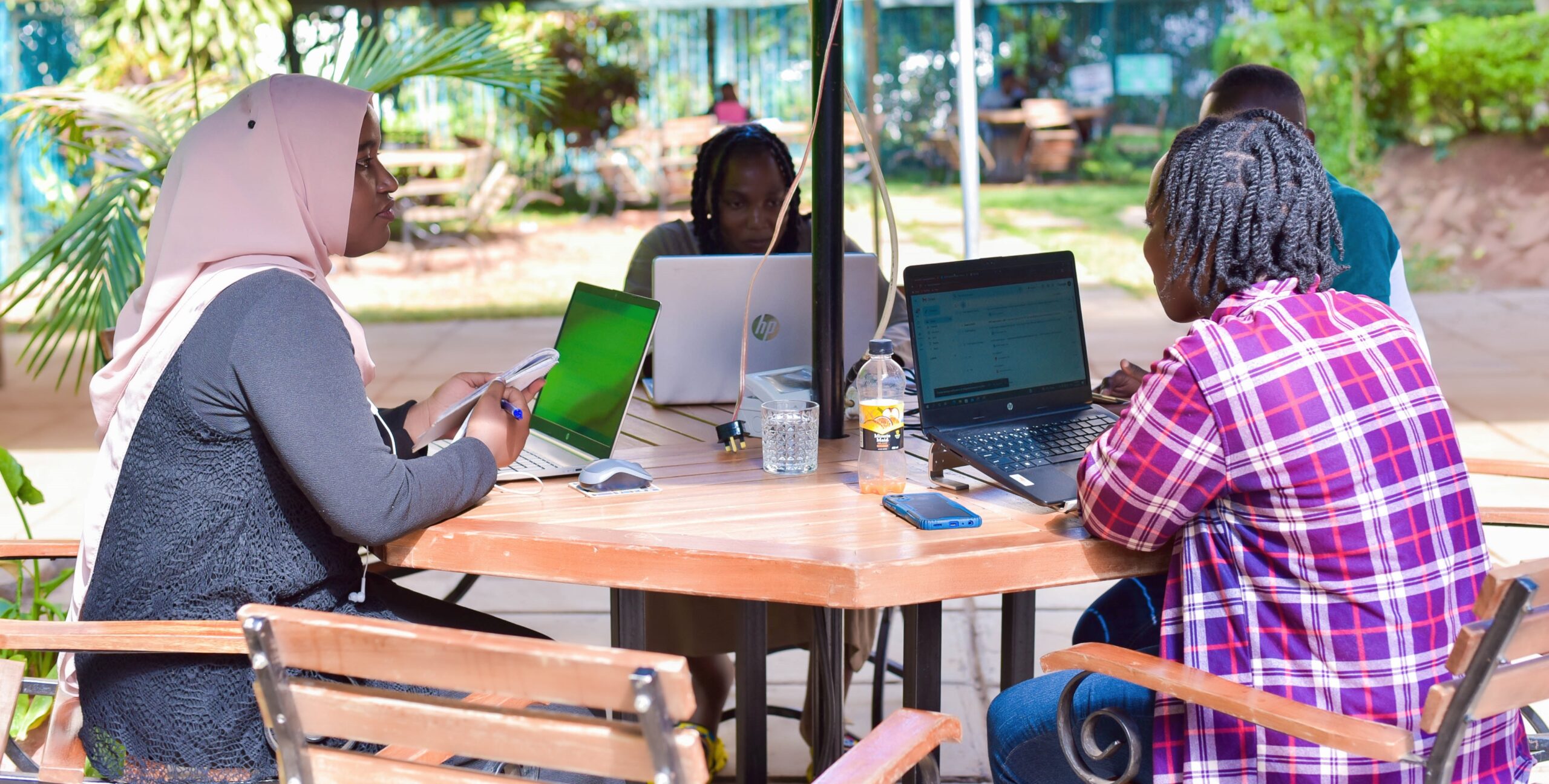 Group of people sitting at outdoor table working on computers